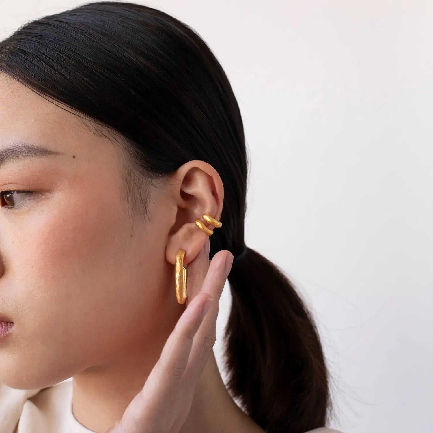 Close-up of a person wearing gold hoop earrings with a plain background